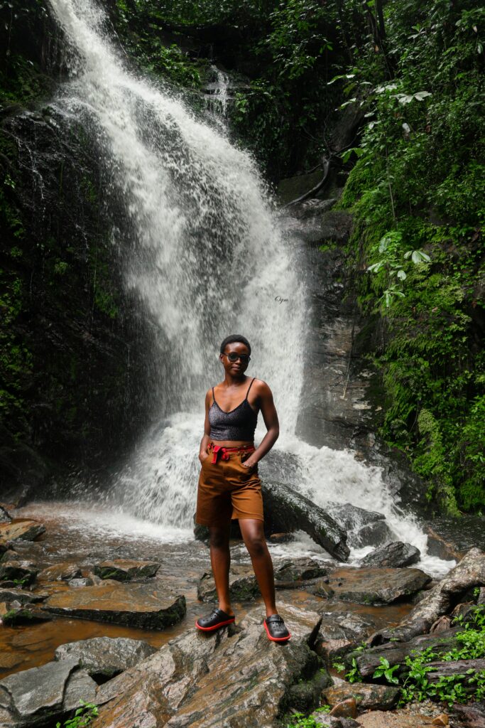 A woman stands confidently in front of a lush waterfall, embodying nature's adventure.