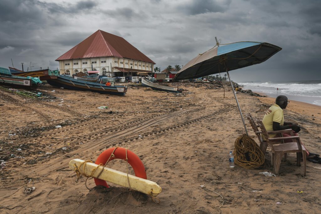 Stormy beach scene with boats, lifeguard, and large building under dark clouds, conveying a moody coastal atmosphere.