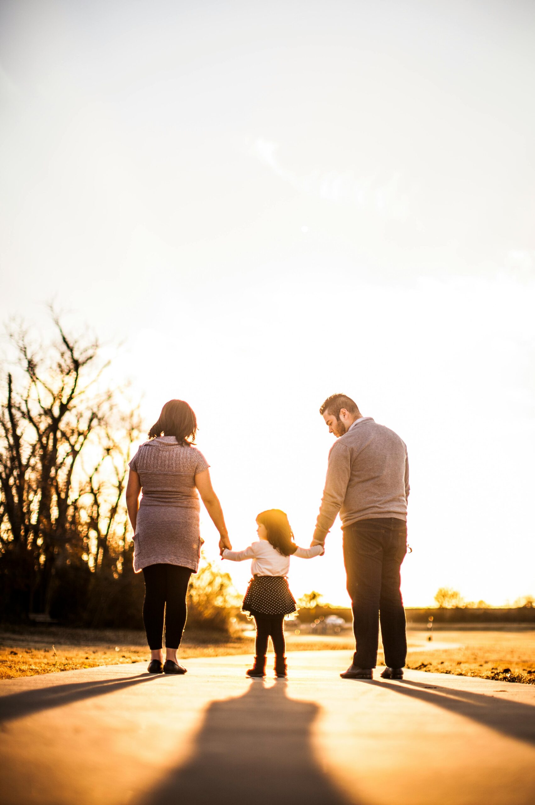 Home A family of three walks hand in hand at sunset, enjoying togetherness and warmth.
