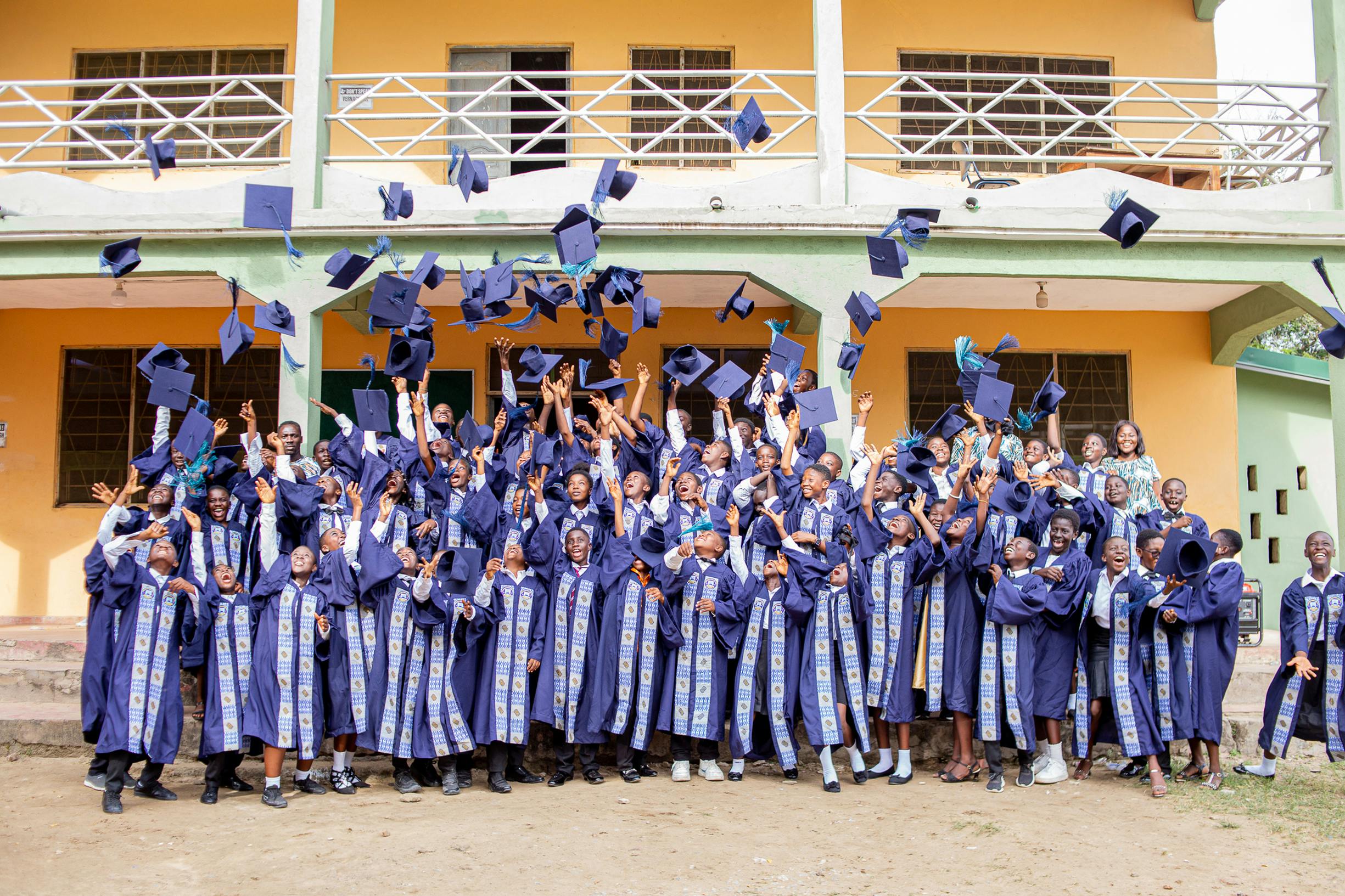Home Group of graduates celebrating by tossing caps outside a building in Winneba, Ghana.